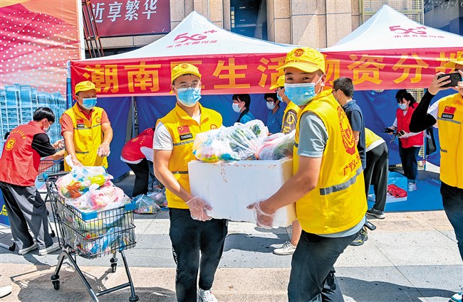 志愿者正分拣、包装分发往各区域的生活物资，并搬运上车。